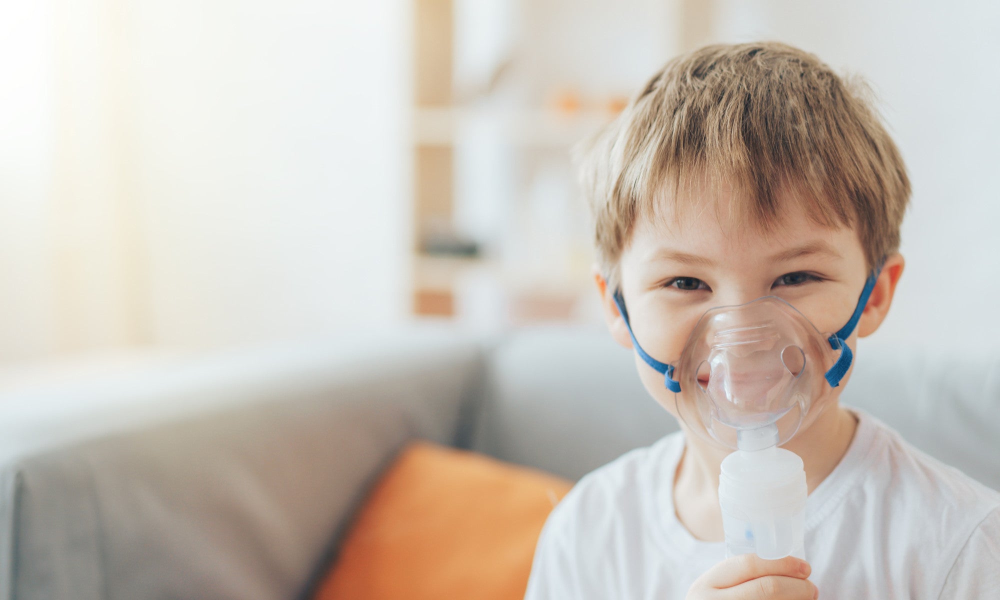 smiling little boy wearing nebulizer mask at home